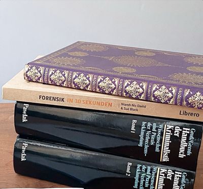 Ein Stapel forensischer Fachbücher auf einem Holztisch.