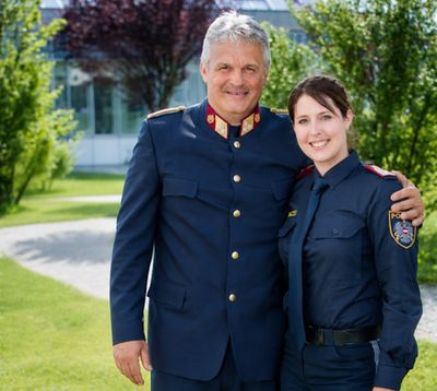 Lisa Dullnig in Polizeiuniform neben ihrem Vater in Uniform vor einem Gebäude im Grünen.