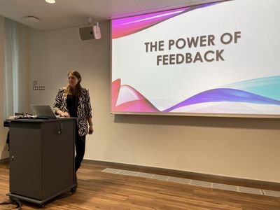 Lisa Dullnig hält einen Vortrag vor einer Leinwand mit dem Titel „The Power of Feedback“.